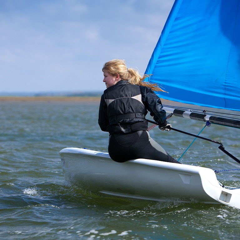 Person sailing on a small boat with a blue sail on an inland lake