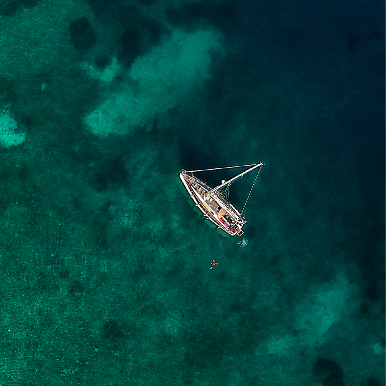 Birdseye view of a boat sailing in shallow clear green waters